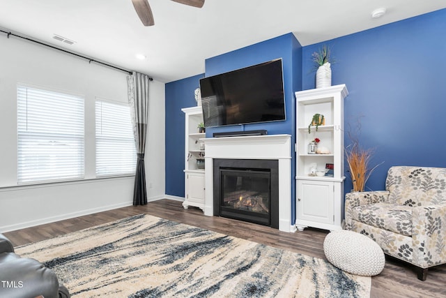 living room featuring baseboards, visible vents, a ceiling fan, a glass covered fireplace, and dark wood-style floors