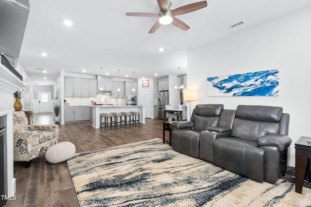 living area featuring ceiling fan with notable chandelier, dark wood finished floors, visible vents, and recessed lighting