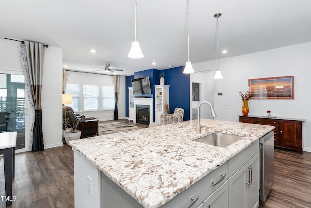 kitchen with a warm lit fireplace, open floor plan, a kitchen island with sink, pendant lighting, and a sink