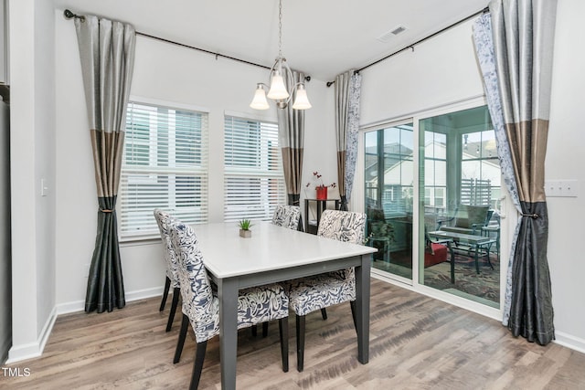 dining space featuring baseboards, wood finished floors, visible vents, and a notable chandelier