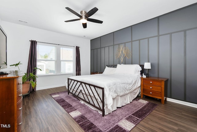 bedroom featuring visible vents, dark wood finished floors, a decorative wall, and baseboards