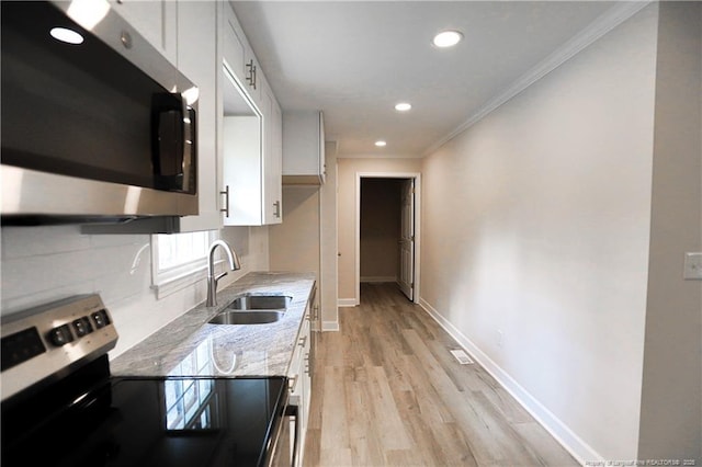 kitchen featuring stainless steel appliances, a sink, ornamental molding, light stone counters, and white cabinetry