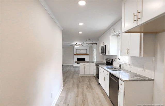 kitchen featuring stainless steel appliances, a sink, open floor plan, white cabinetry, and light stone counters