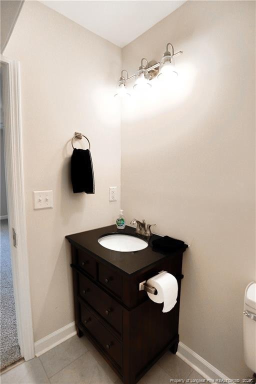 half bathroom featuring tile patterned flooring, vanity, toilet, and baseboards