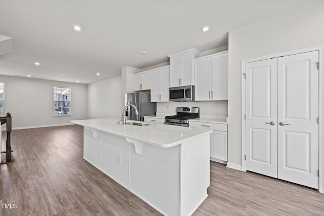 kitchen featuring white cabinets, an island with sink, a sink, baseboards, and appliances with stainless steel finishes