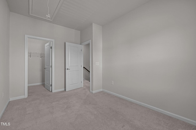 unfurnished bedroom featuring a closet, attic access, a spacious closet, light colored carpet, and baseboards