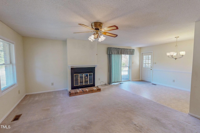 unfurnished living room with a brick fireplace, a textured ceiling, ceiling fan with notable chandelier, and light colored carpet