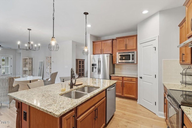 kitchen with a center island with sink, stainless steel appliances, tasteful backsplash, light wood-style floors, and a sink