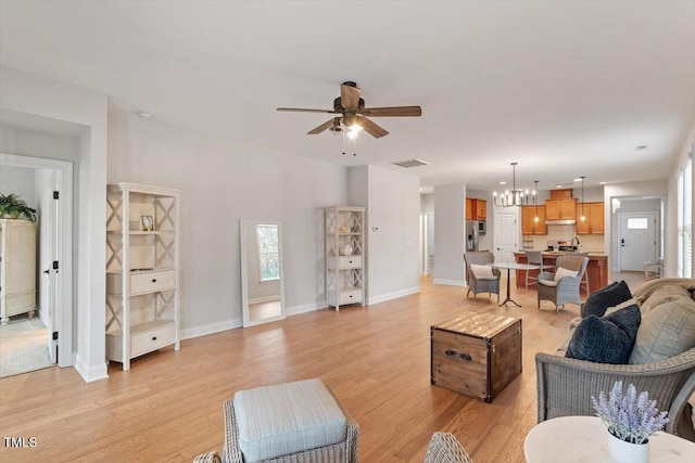 living area featuring visible vents, light wood-style flooring, baseboards, and ceiling fan with notable chandelier