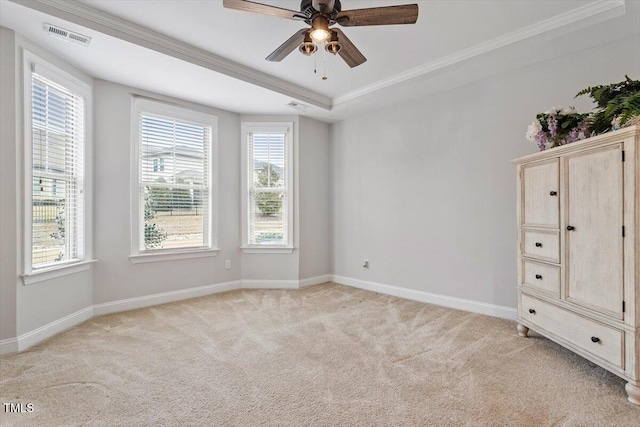 empty room featuring baseboards, a raised ceiling, a ceiling fan, light colored carpet, and ornamental molding