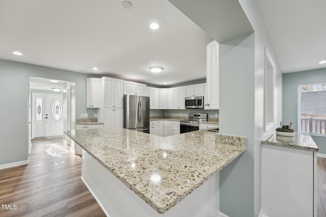 kitchen with stainless steel appliances, wood finished floors, white cabinetry, and light stone countertops