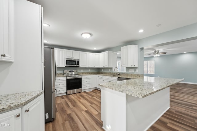 kitchen with a peninsula, appliances with stainless steel finishes, wood finished floors, and white cabinets