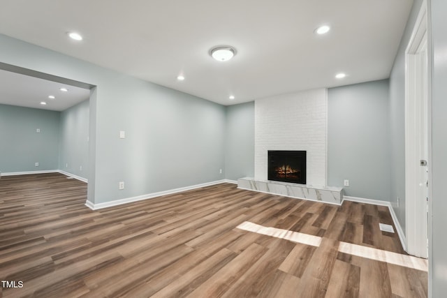 unfurnished living room with a large fireplace, baseboards, wood finished floors, and recessed lighting