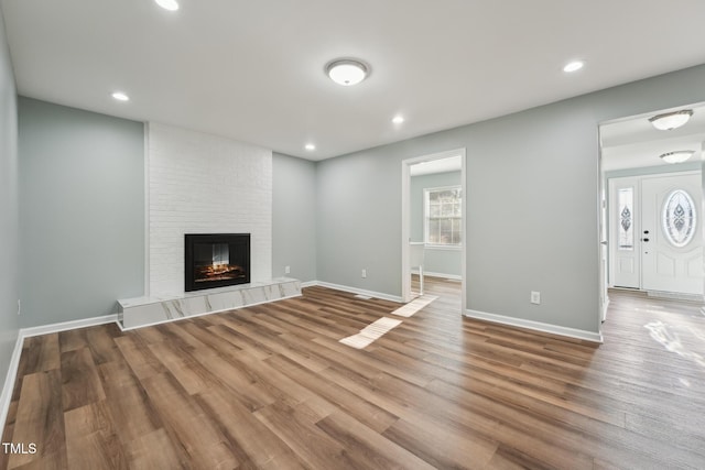 unfurnished living room featuring recessed lighting, baseboards, a tiled fireplace, and wood finished floors