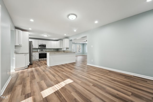 kitchen with baseboards, white cabinets, light wood-style flooring, open floor plan, and stainless steel appliances