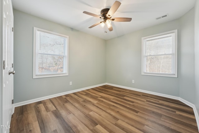 empty room with a wealth of natural light, baseboards, visible vents, and wood finished floors