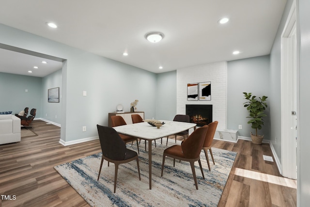 dining space with recessed lighting, a large fireplace, baseboards, and wood finished floors