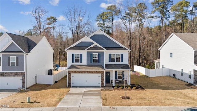 view of front of house with driveway, stone siding, an attached garage, fence, and a front yard