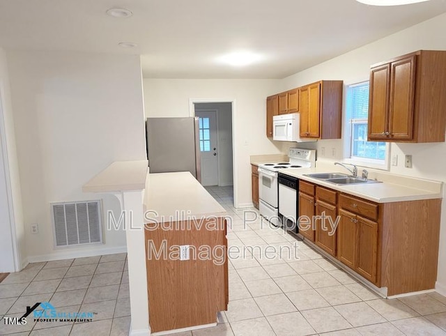 kitchen featuring brown cabinets, light countertops, visible vents, a sink, and white appliances