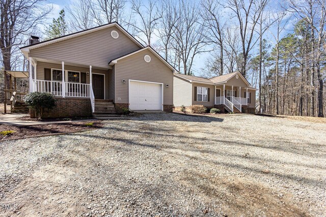 ranch-style house featuring a garage, covered porch, and gravel driveway