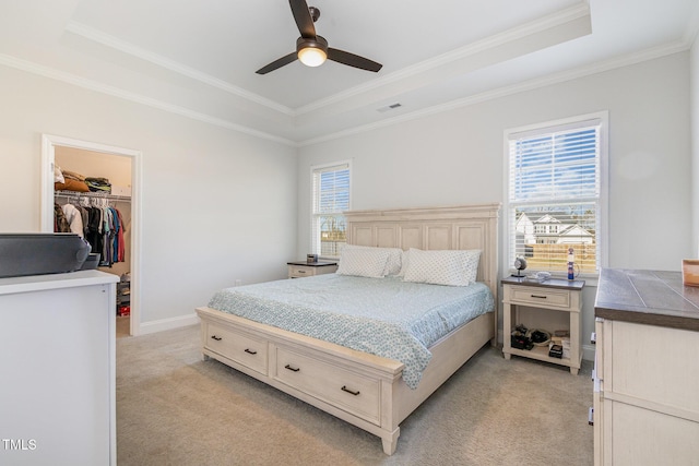 bedroom with a tray ceiling, multiple windows, light colored carpet, and a walk in closet