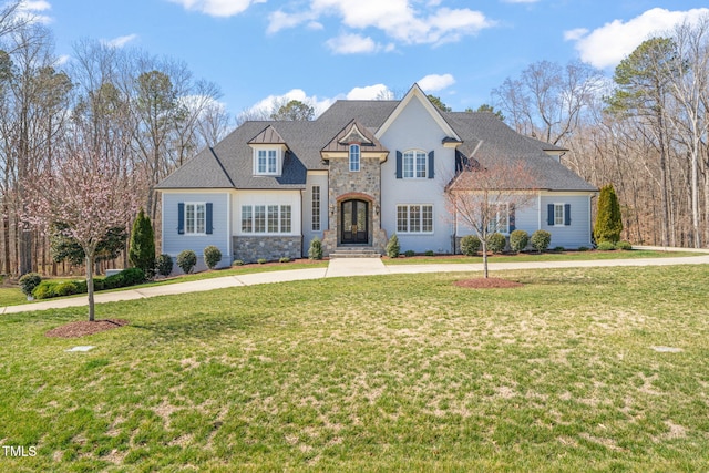 french country style house with stone siding, curved driveway, and a front lawn