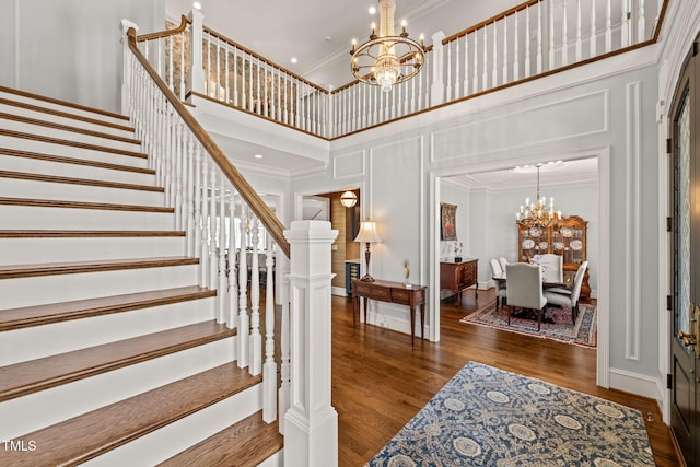 staircase with wood finished floors, a chandelier, crown molding, and a decorative wall