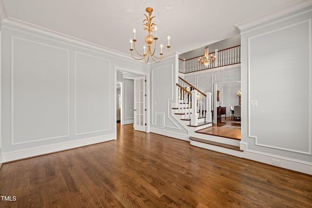 foyer with a notable chandelier, wood finished floors, stairway, crown molding, and a decorative wall