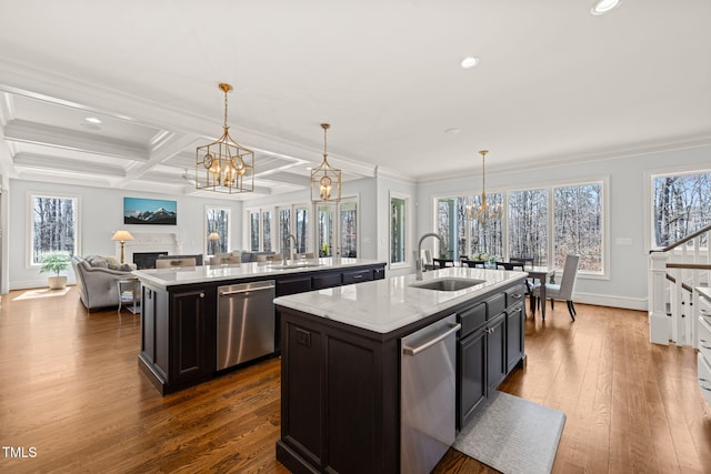 kitchen featuring an island with sink, a sink, stainless steel dishwasher, an inviting chandelier, and a fireplace