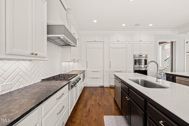 kitchen with custom exhaust hood, appliances with stainless steel finishes, white cabinetry, and a sink