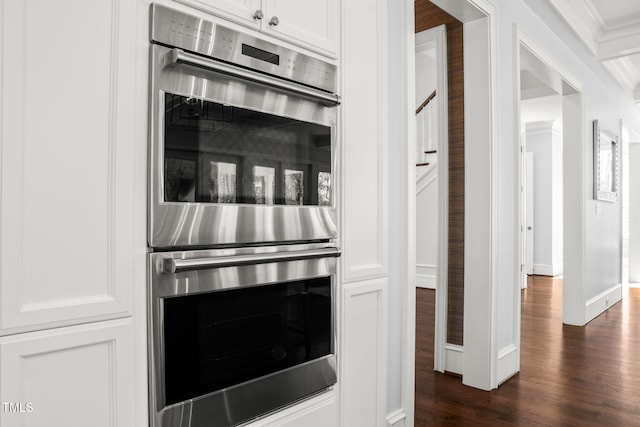 kitchen featuring baseboards, dark wood finished floors, ornamental molding, stainless steel double oven, and white cabinetry