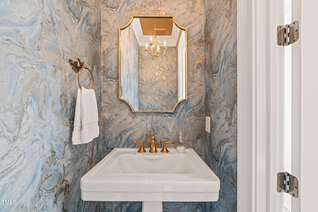 bathroom with a sink, a chandelier, and wallpapered walls