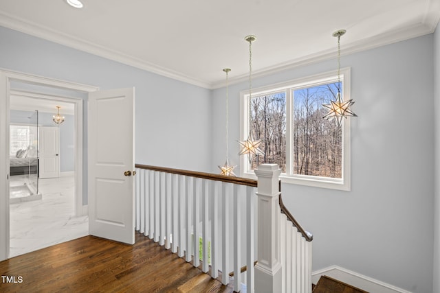 hallway featuring baseboards, dark wood-style flooring, crown molding, a notable chandelier, and an upstairs landing