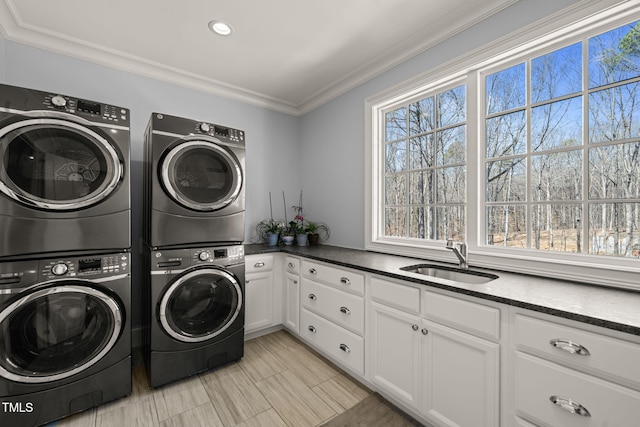 laundry room featuring washer and clothes dryer, a sink, stacked washing maching and dryer, cabinet space, and crown molding