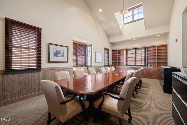 dining space featuring a wainscoted wall, light carpet, high vaulted ceiling, wooden walls, and a skylight