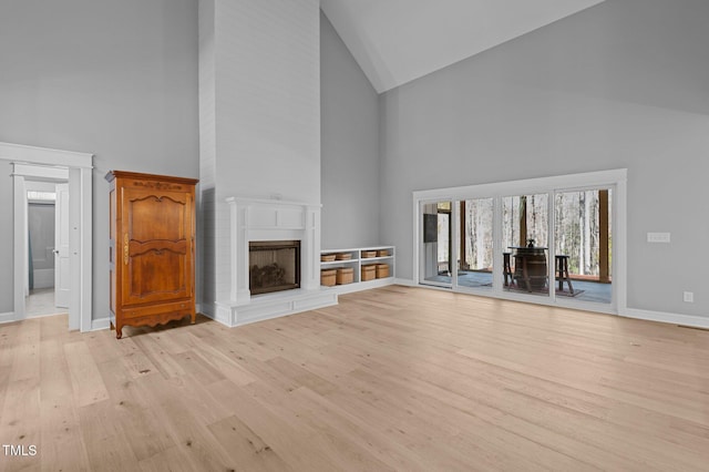 unfurnished living room featuring light wood finished floors, a fireplace with raised hearth, high vaulted ceiling, and baseboards