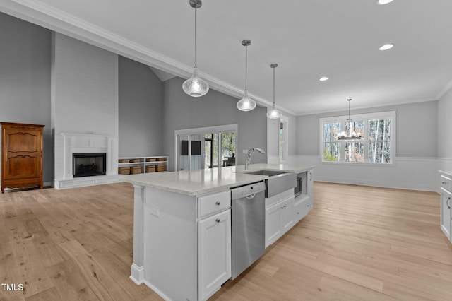 kitchen featuring a wainscoted wall, a fireplace with raised hearth, a sink, stainless steel appliances, and light wood finished floors