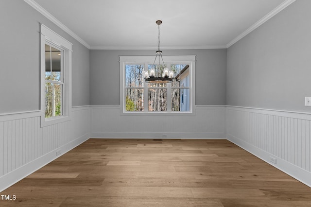 unfurnished dining area with an inviting chandelier, ornamental molding, wood finished floors, and wainscoting