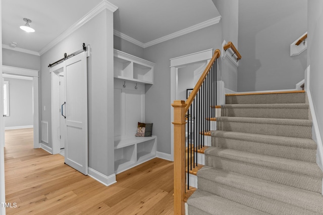 mudroom featuring baseboards, light wood-type flooring, a barn door, and ornamental molding