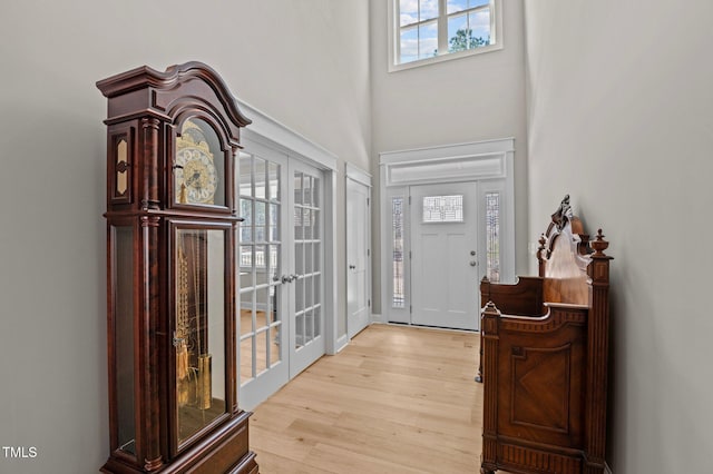 entrance foyer with a towering ceiling, light wood-style floors, and french doors