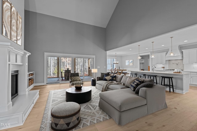 living area featuring a fireplace with raised hearth, a chandelier, recessed lighting, a high ceiling, and light wood-style floors