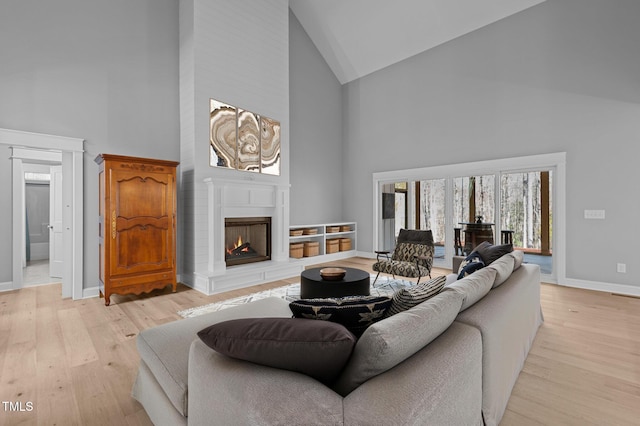 living room with light wood-style floors, baseboards, a warm lit fireplace, and high vaulted ceiling