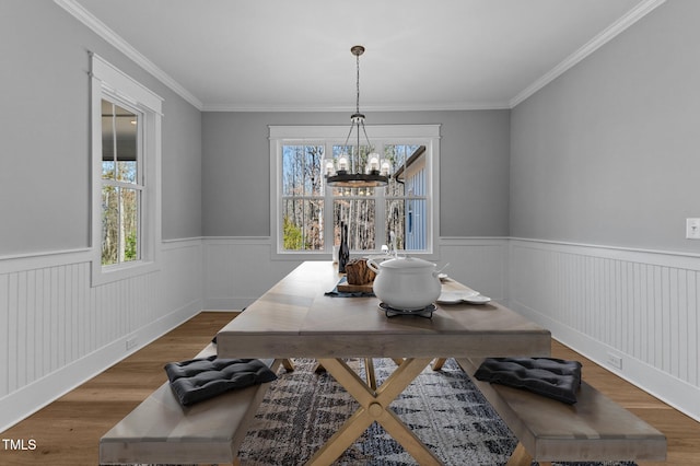 dining space with a notable chandelier, wood finished floors, wainscoting, and crown molding