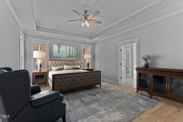 bedroom with baseboards, a raised ceiling, light wood-style flooring, and crown molding