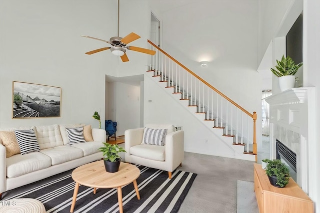 carpeted living area with ceiling fan, a premium fireplace, a towering ceiling, and stairs