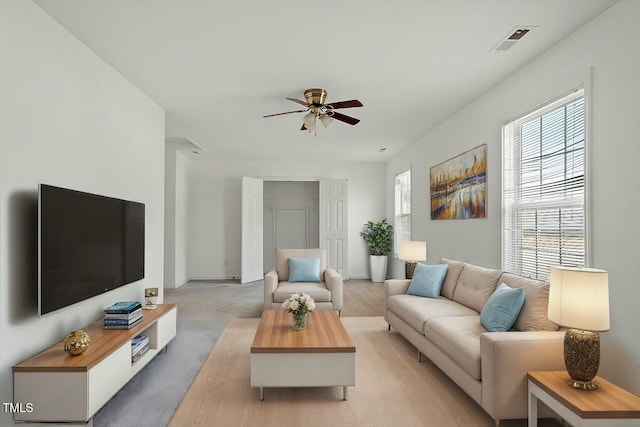 living room featuring visible vents, light colored carpet, and ceiling fan