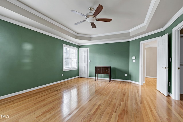 spare room featuring baseboards, a ceiling fan, a tray ceiling, crown molding, and light wood-style floors