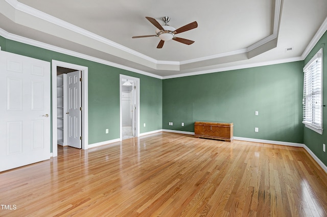 empty room with baseboards, a tray ceiling, and light wood-style floors