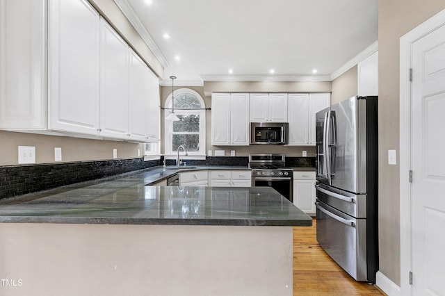 kitchen featuring crown molding, light wood finished floors, appliances with stainless steel finishes, a sink, and a peninsula