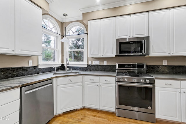 kitchen with white cabinets, ornamental molding, decorative light fixtures, stainless steel appliances, and a sink